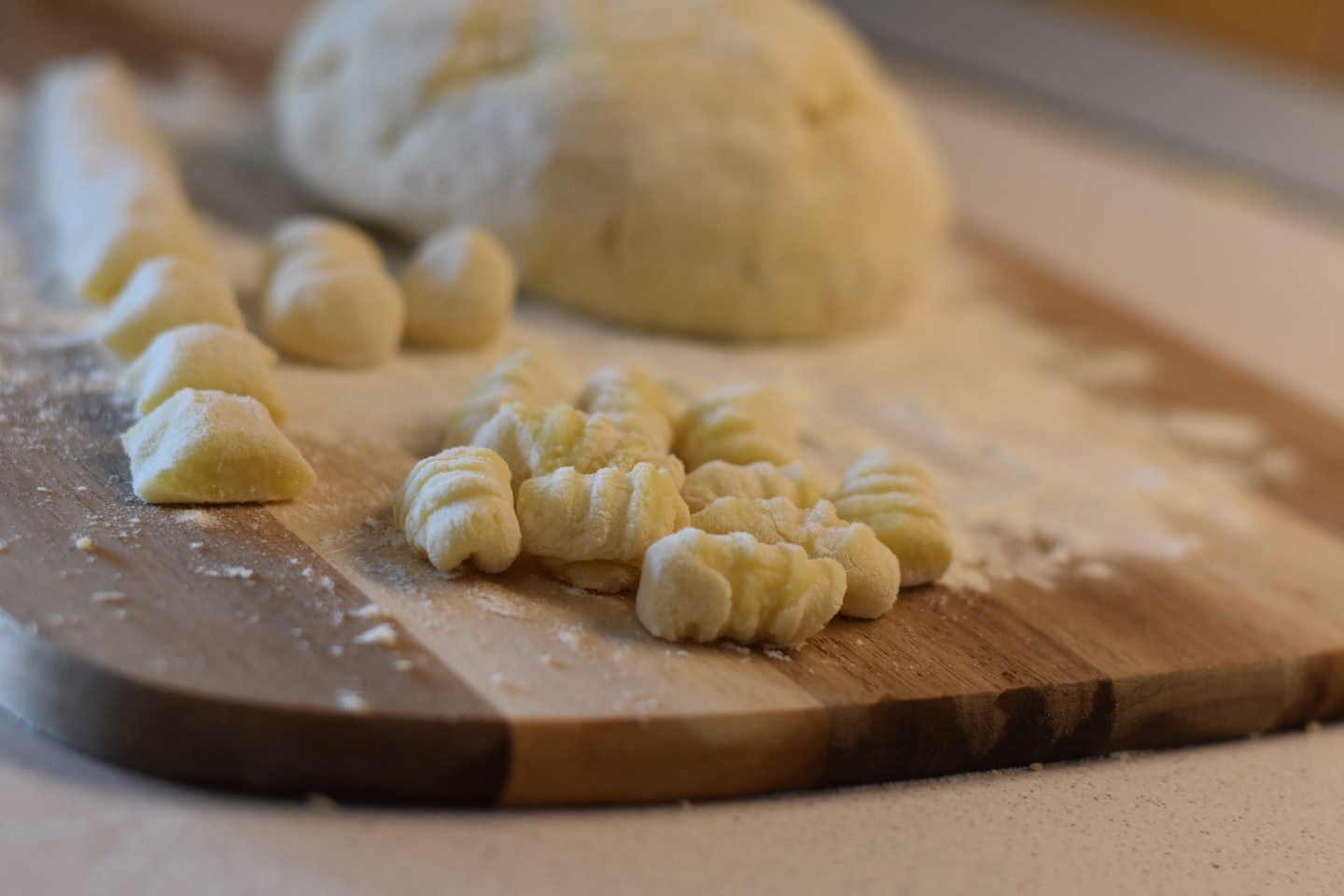 Uncooked gnocchi dusted with flour on a wooden board.