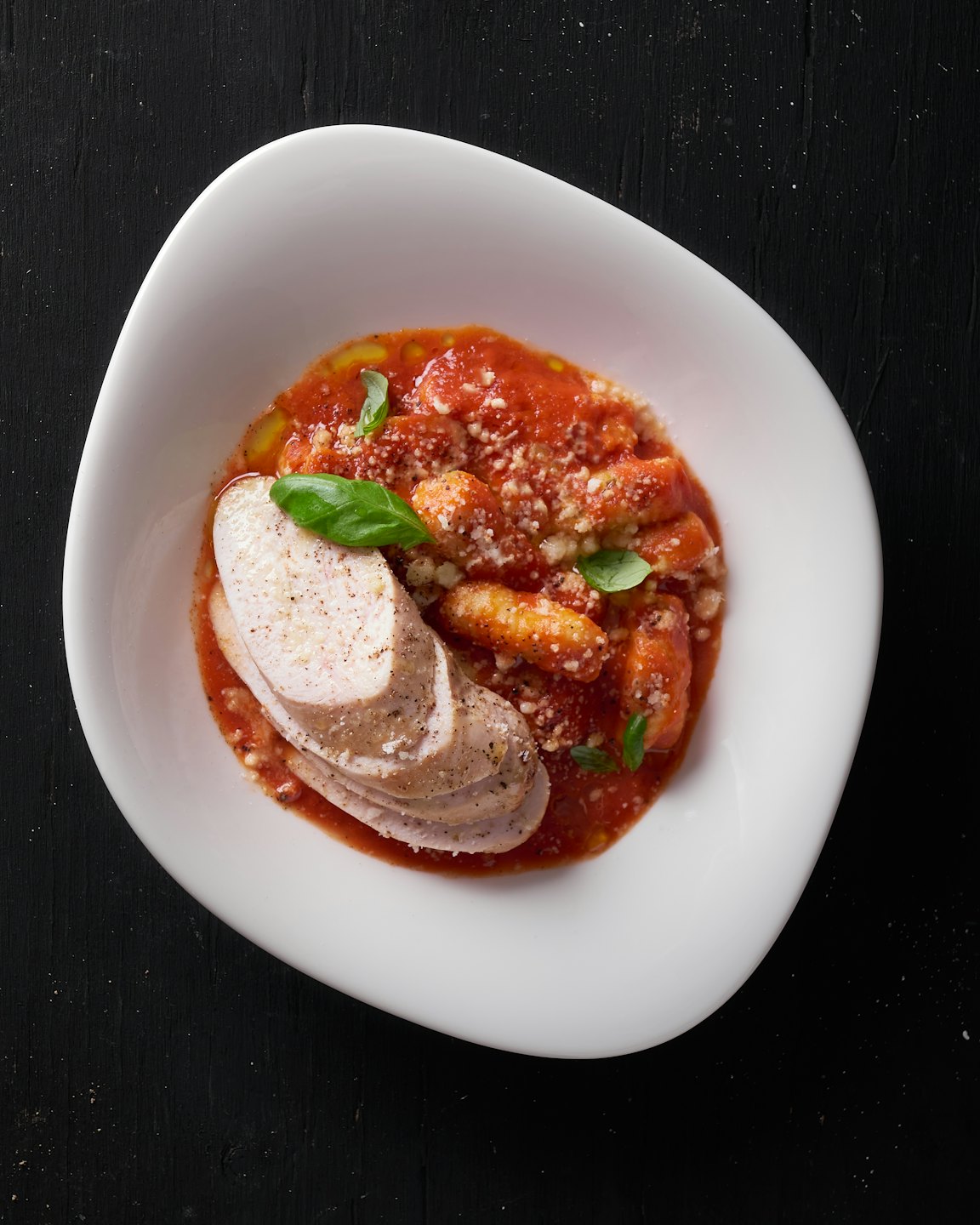 Gnocchi with tomato sauce, cheese, basil, and chicken in a bowl.