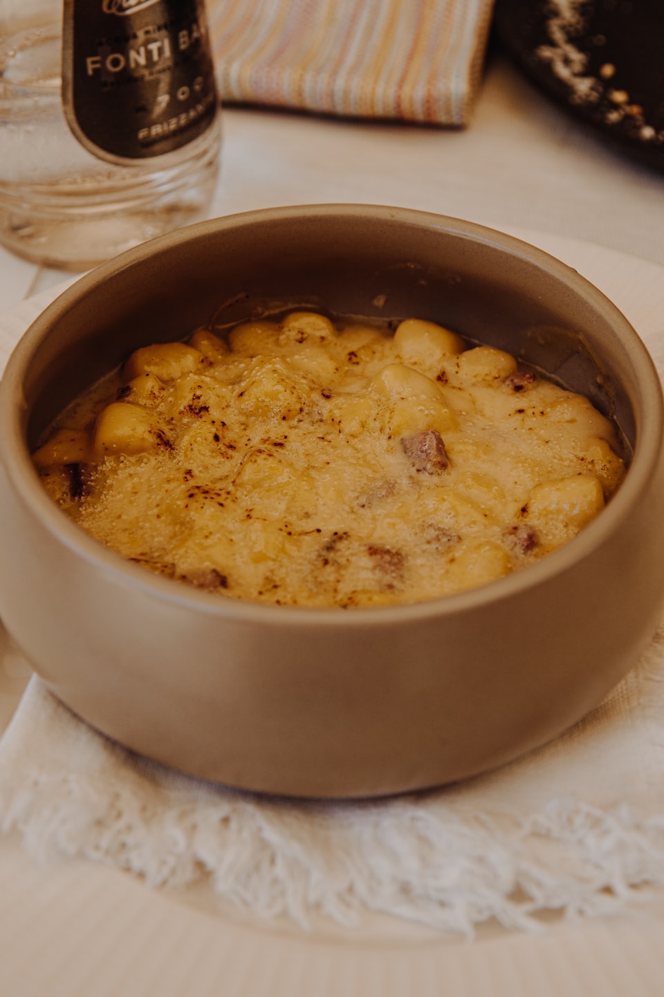 Baked gnocchi topped with cheese and meat in a ceramic bowl.