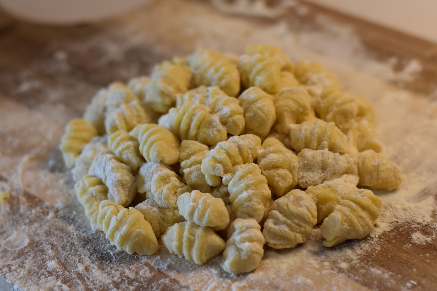 Freshly made potato gnocchi covered in flour on a wooden board.